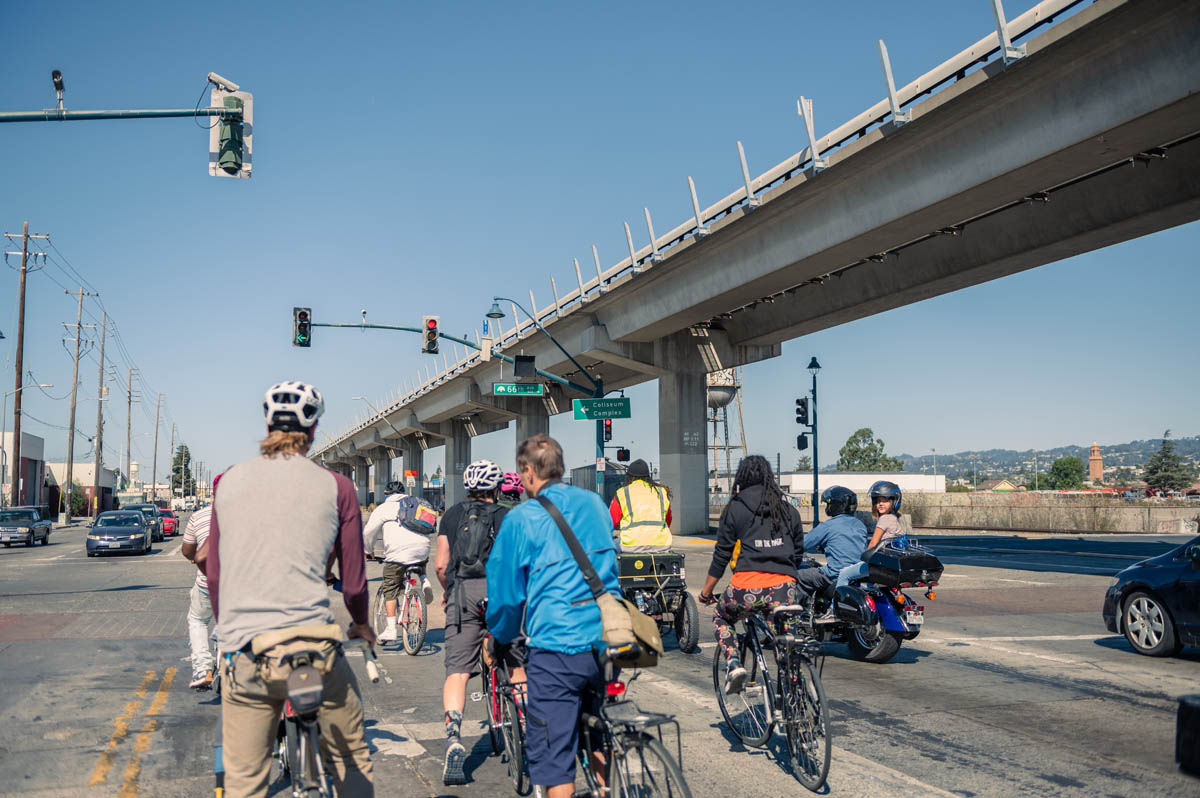 cyclists sit under bart tracks overhead in a big intersection