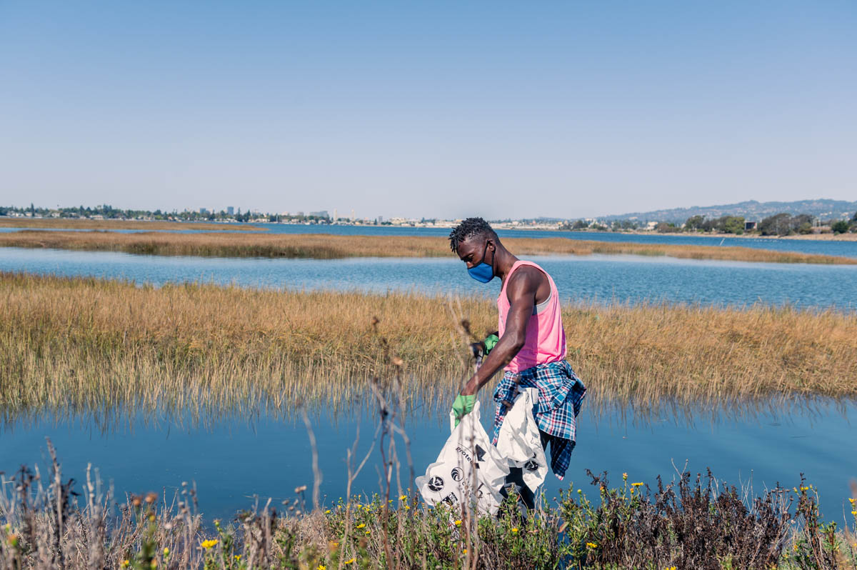 guy in pink shirt cleans trash from shore