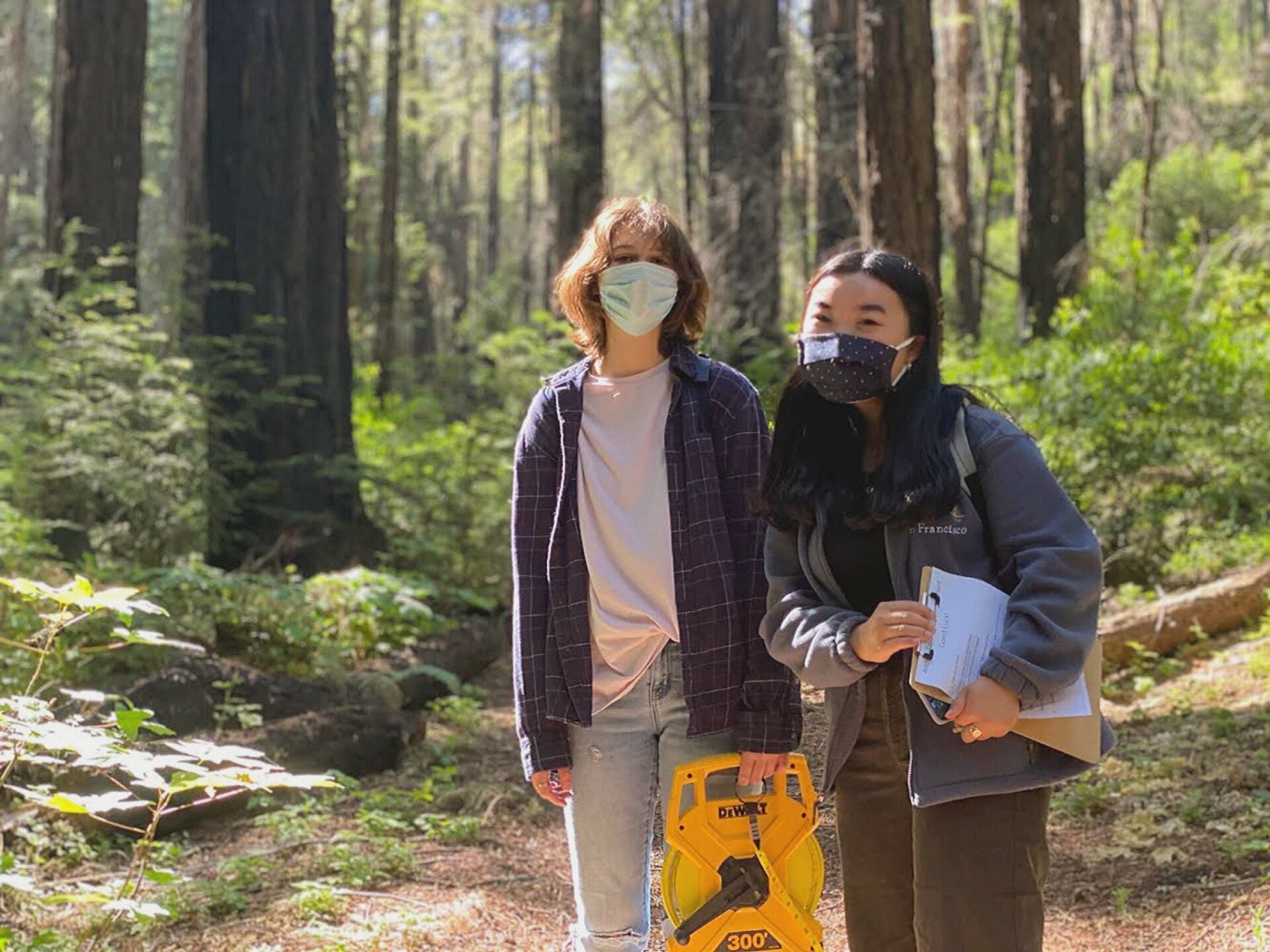 Two teenage girls wearing masks in a forest.