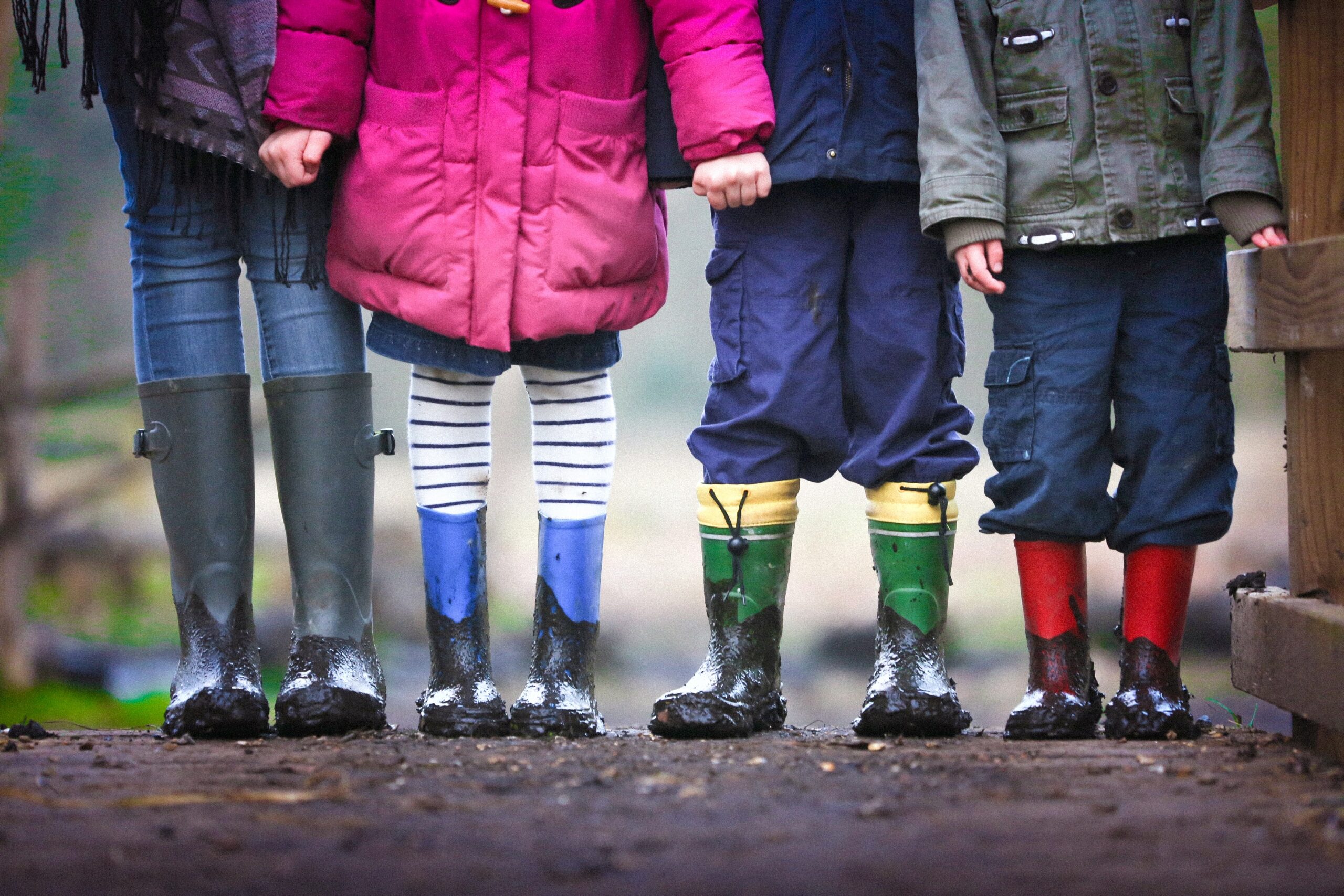 Four children in rainboots standing in a line from chests down.