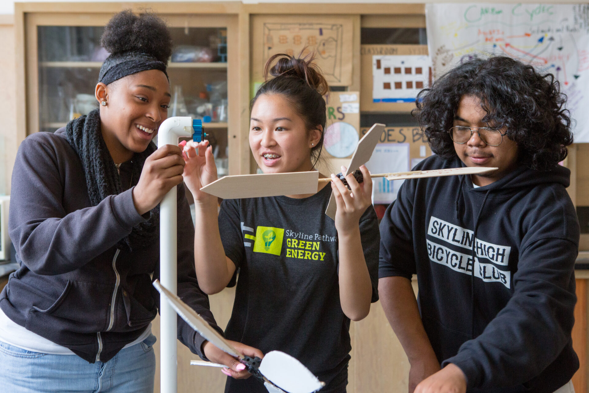 Three students build a windmill in a science lab.